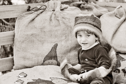 Must-valge pilt päkapiku mütsiga lapsest, kes istub suurte kingikottide juures.